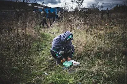 Un inmigrante afgano come junto a la cola de gente que recibe comida de las asociaciones de ayuda a los inmigrantes de Calais