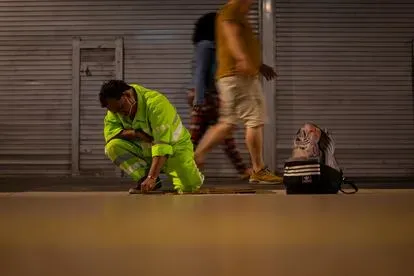 Dos transeúntes caminan en la madrugada mientras Félix quita chicles del suelo.