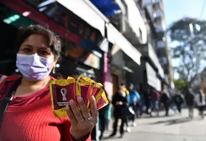 Una mujer muestra los sobres de figuristas que acaba de comprar en un kiosco del barrio de Boedo, en Buenos Aires, el 13 de septiembre de 2022. Detrás, la fila de la gente que esperas su turno.