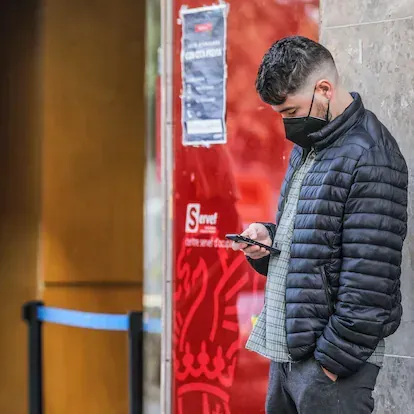 Un joven mira su teléfono móvil mientras espera para entrar en una oficina del SEPE (antiguo INEM), en Valencia, Comunidad Valenciana (España), a 12 de febrero de 2021. El número de parados registrado