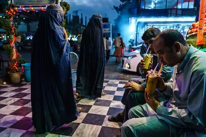 Dos afganas cubiertas totalmente con el burka pasan en Kabul ante unos hombres que disfrutan de un batido, el 20 de agosto de 2021.