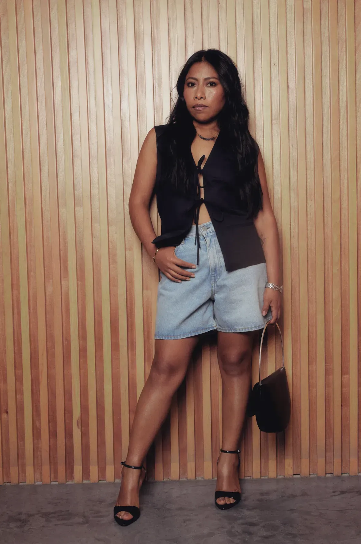 Yalitza Aparicio lleva bermudas de mezclilla con un top negro de moños y sandalias de tacón...