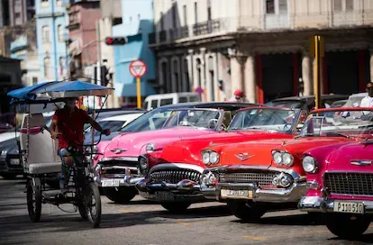 Un bicitaxi pasa frente a varios coches clásicos que esperan clientes, el 27 de enero, en el Parque Central de La Habana, Cuba.