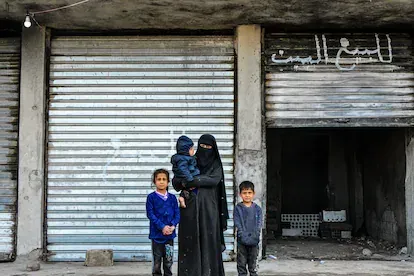 Malika Jadr Abdallah, de 30 años, posa junto a sus hijos frente a su casa. Pudo volver un mes y medio después de que terminaran los combates en Gewayran, debido a la cercanía de su hogar y la prisión.
