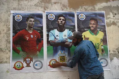 Un hombre pega carteles de Cristiano Ronaldo, Lionel Messi y Neymar con las camisetas de sus selecciones en un muro de Karachi, en Pakistán.