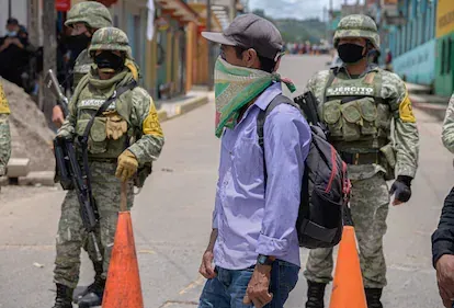 Un integrante de la autodefensa El machete camina frete a miembros del Ejército mexicano.