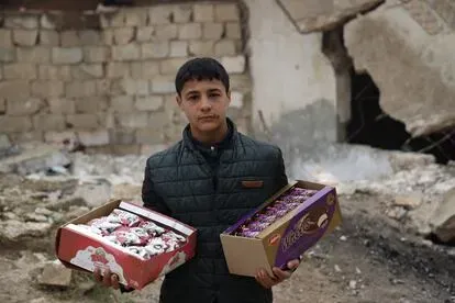 Hussein Mutawa, de 12 años, frente a un edificio destruido en su pueblo de Sarmin, en el campo de Idlib, mientras deambula por las inseguras calles de la ciudad para vender galletas. Hussein dejó la e