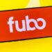 The Fubo logo on a cell phone on a yellow background.