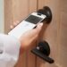 Hands hold a phone key pass up to a Level Lock Pro on a wood door.