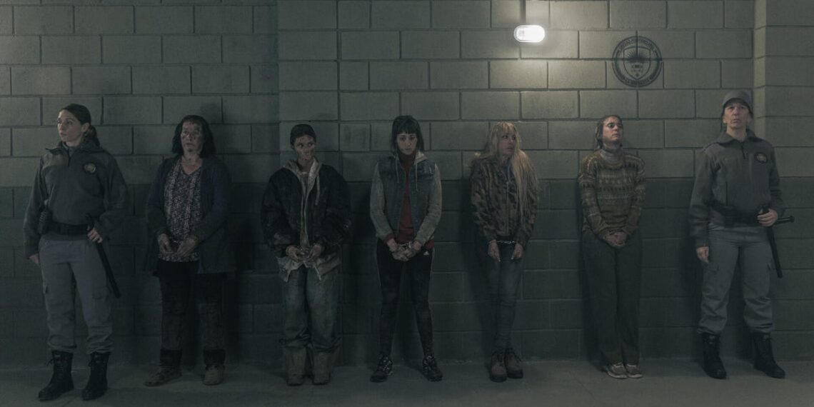 A group of female prisoners stand handcuffed in front of a wall