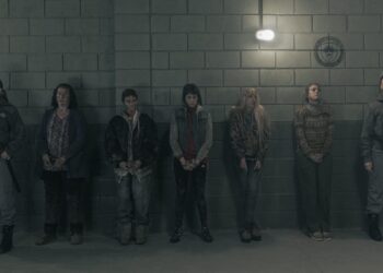 A group of female prisoners stand handcuffed in front of a wall