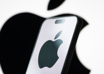 In this photo illustration, the logo of Apple Inc. is displayed on a smartphone screen, with the company's iconic black apple symbol visible in the background.