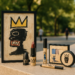 A lipstick tube that reads Basquiat and a cap that is shaped like a crown.